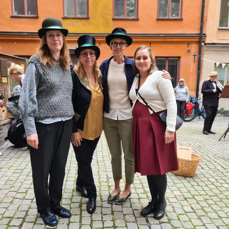Fyra kvinnor i plommonstop på en kullerstensgata i Gamla Stan
