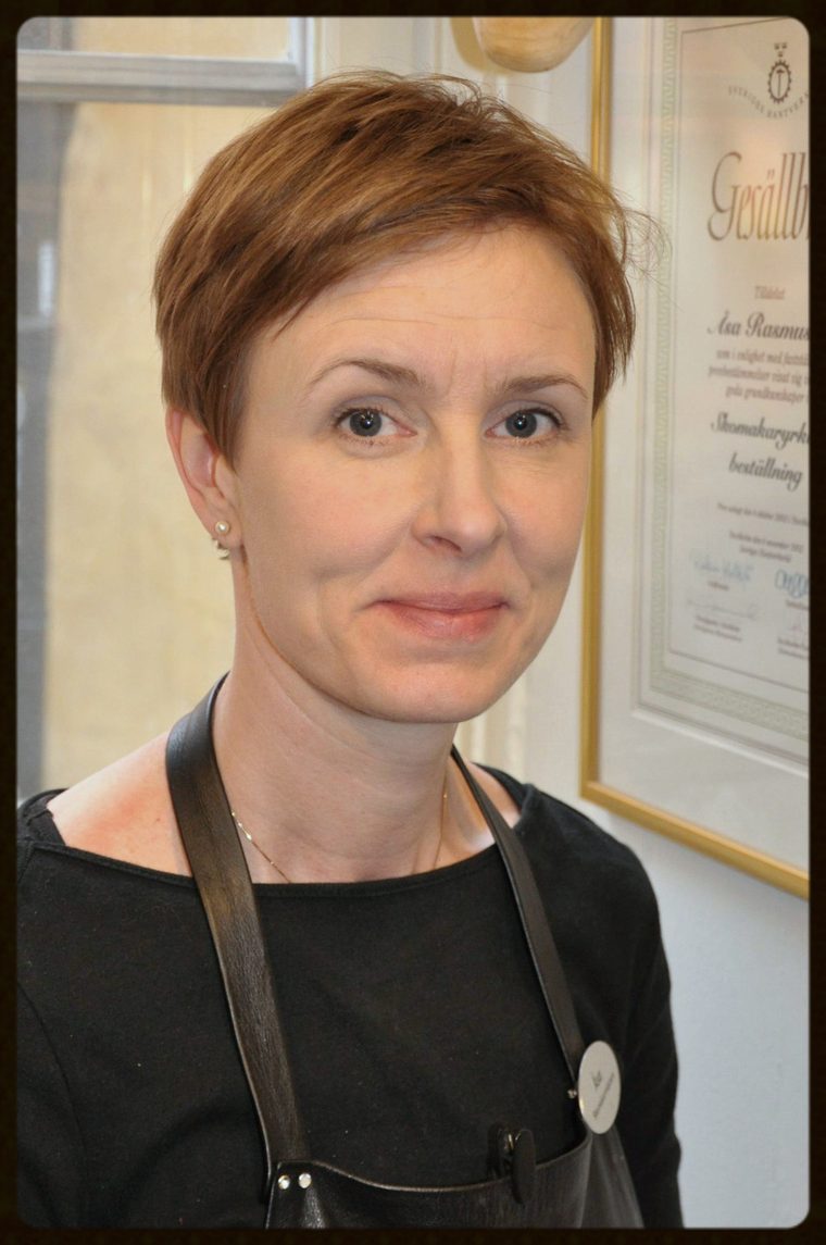 Åsa Rasmussen i läderförkläde framför sitt inramade gesällbrev