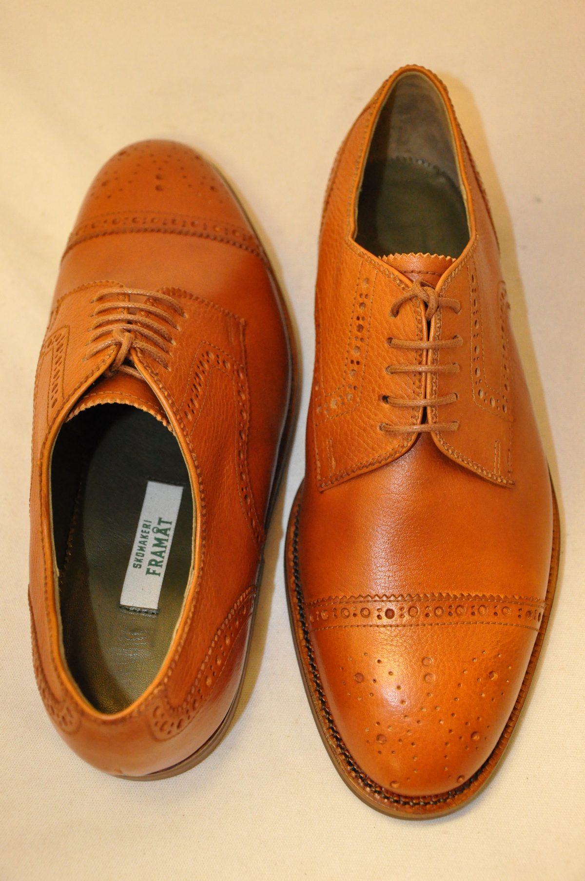 Ett par färdiga ljusbruna brogues uppifrån med Skomakeri Framåts etikett i bindsulan