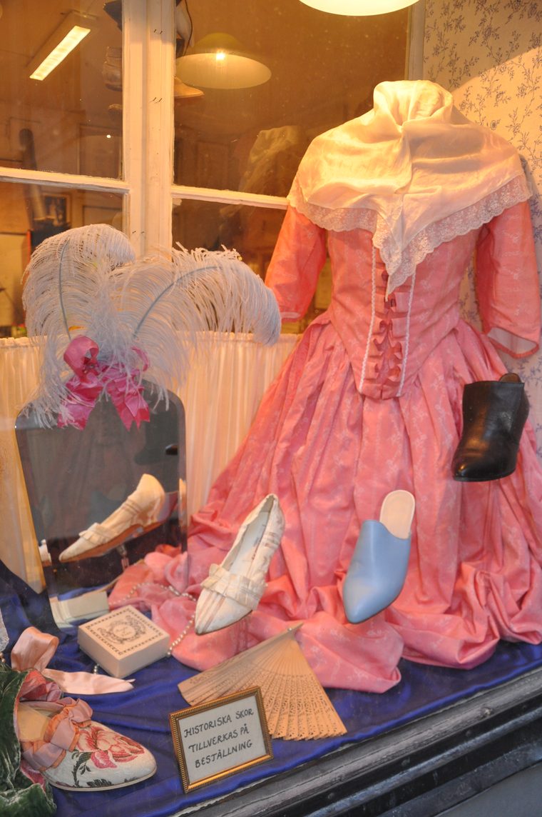 Skyltfönster med rosa 1700-talsklänning, plymer och pastellfärgade historiska skor